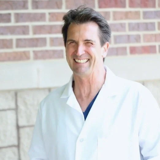Dr. Stephen Forrest, DDS, smiling in a white coat in front of a brick wall.