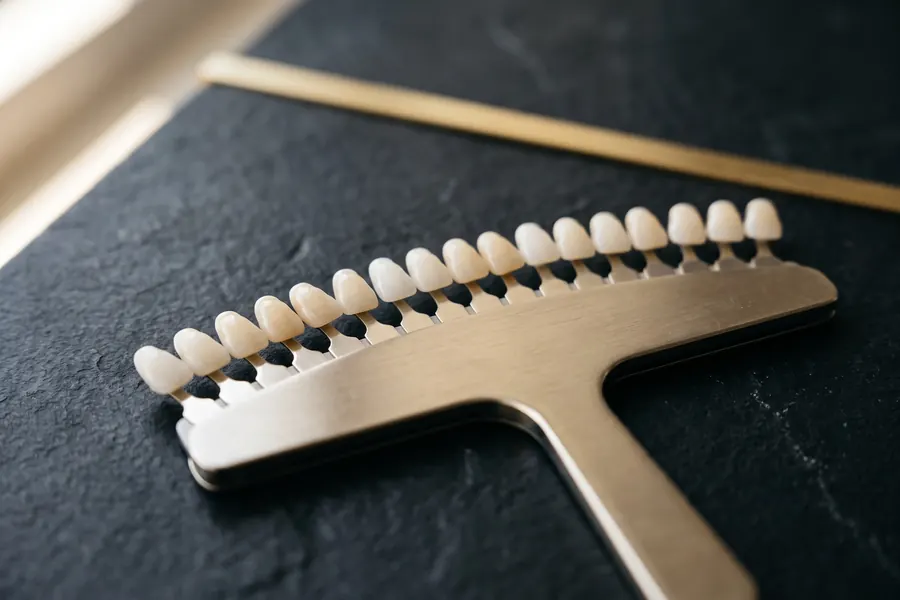 A porcelain shade guide of tooth-colored tabs on a dark stone surface in warm light.